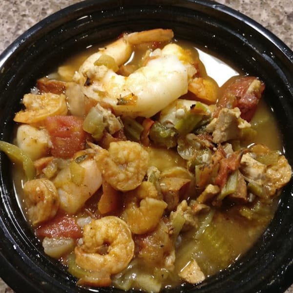 Soul food gumbo with shrimp, sausage, and vegetables in a black bowl.