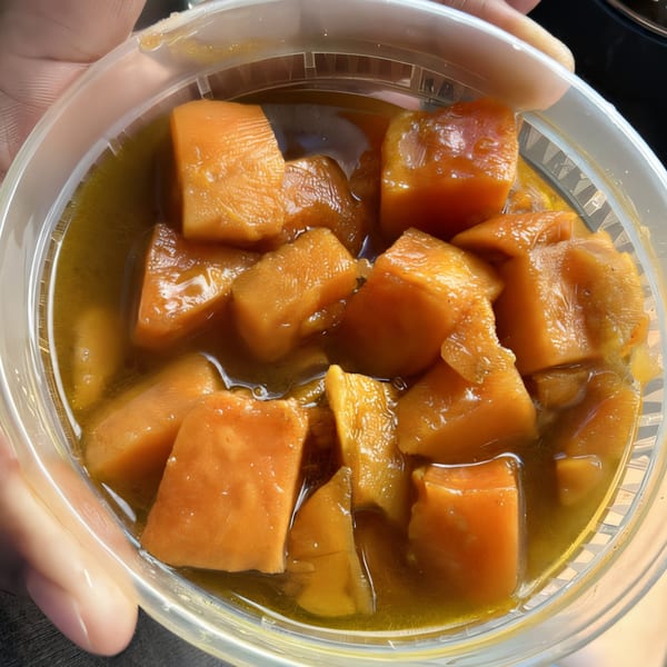 Close-up of candied yams in a clear plastic container, held by a hand.