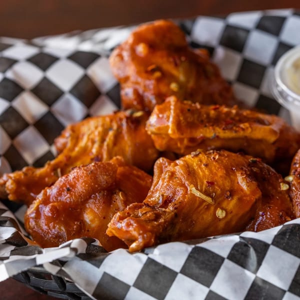 Close-up of Blazing Chicken Shack II's saucy chicken wings in a checkered paper-lined basket.