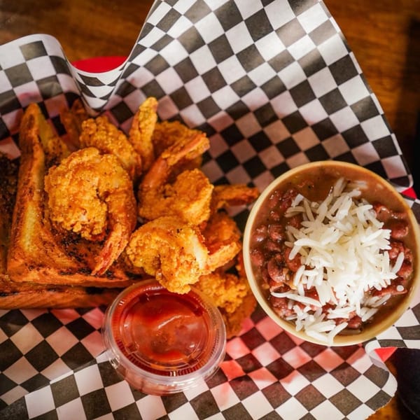 Fried shrimp, Texas toast, red beans and rice, and dipping sauce in a checkered basket.