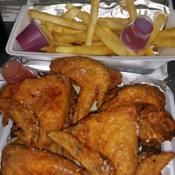 Golden fried chicken wings and french fries with dipping sauces in takeout containers.