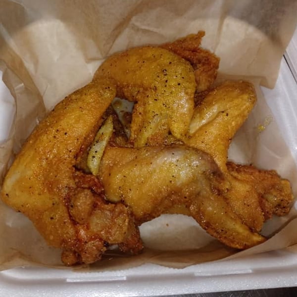 Golden-brown fried chicken wings, seasoned with pepper, served in a white takeout container with parchment paper.