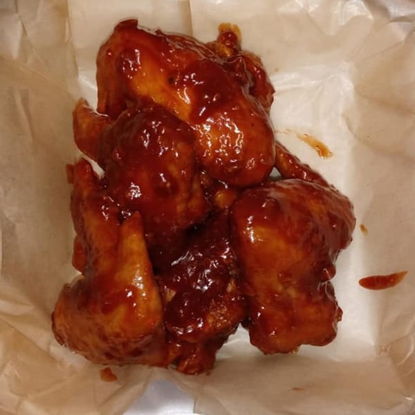 Several Blazing Chicken Shack II chicken wings, coated in a glistening, dark red sauce, rest on parchment paper.