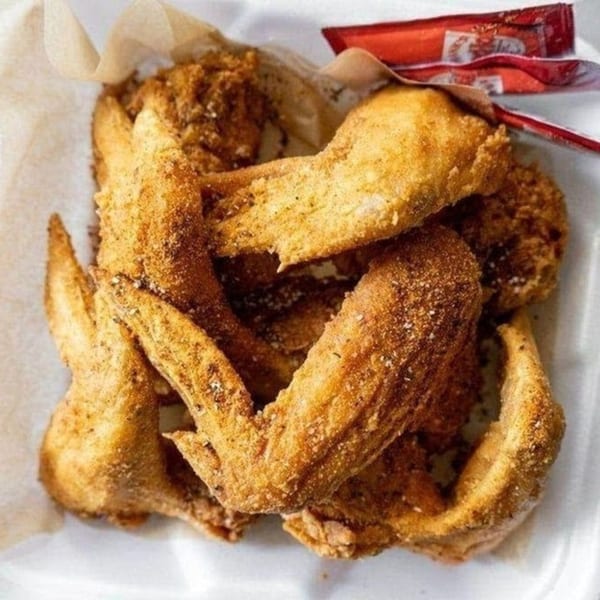 Crispy fried chicken wings with seasoning in a white container with red sauce packets.